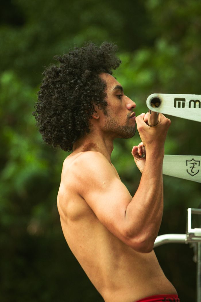 Fit man with curly hair performing a pull-up outdoors, showcasing strength and fitness.